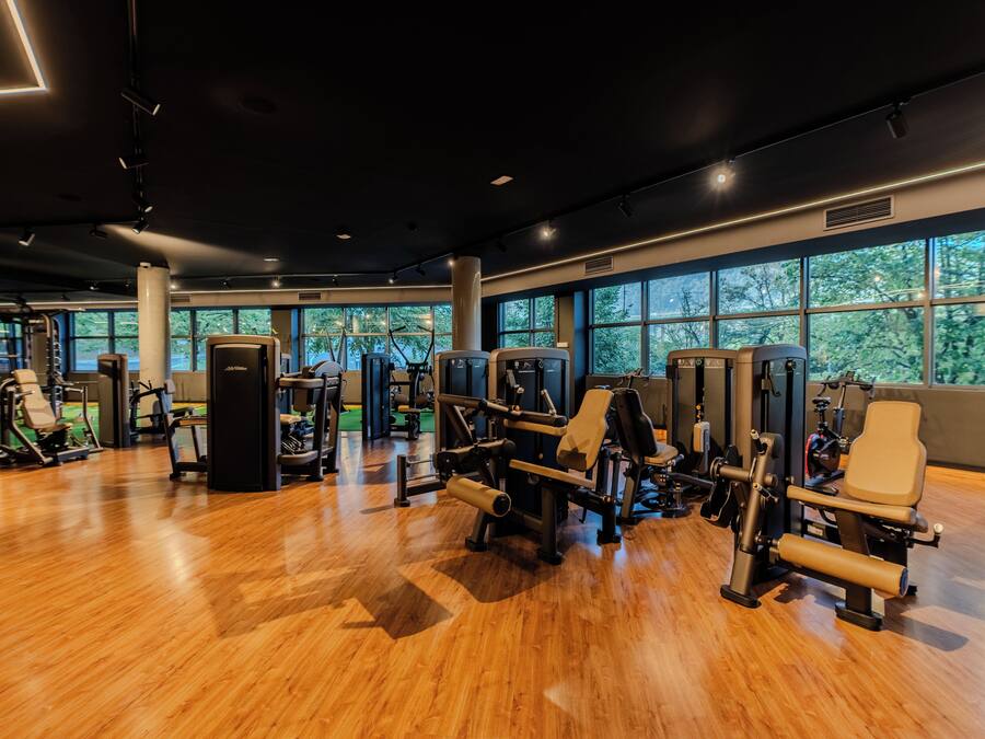 Un gimnasio con diversas máquinas de ejercicio, amplias ventanas y suelo de madera.