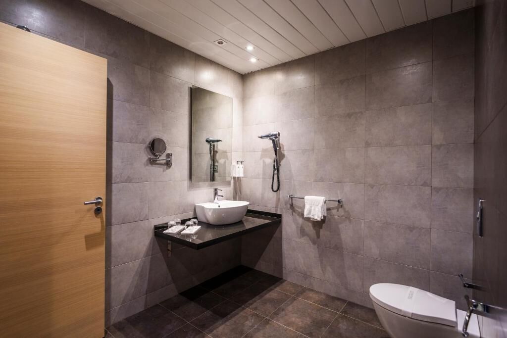 Un baño moderno con puerta de madera, espejo redondo, lavamanos e inodoro.