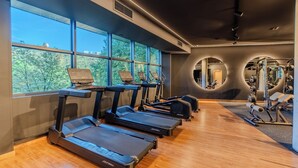 Un gimnasio con cintas de correr, equipamiento de ejercicio y ventanas amplias que dan a vistas de árboles.