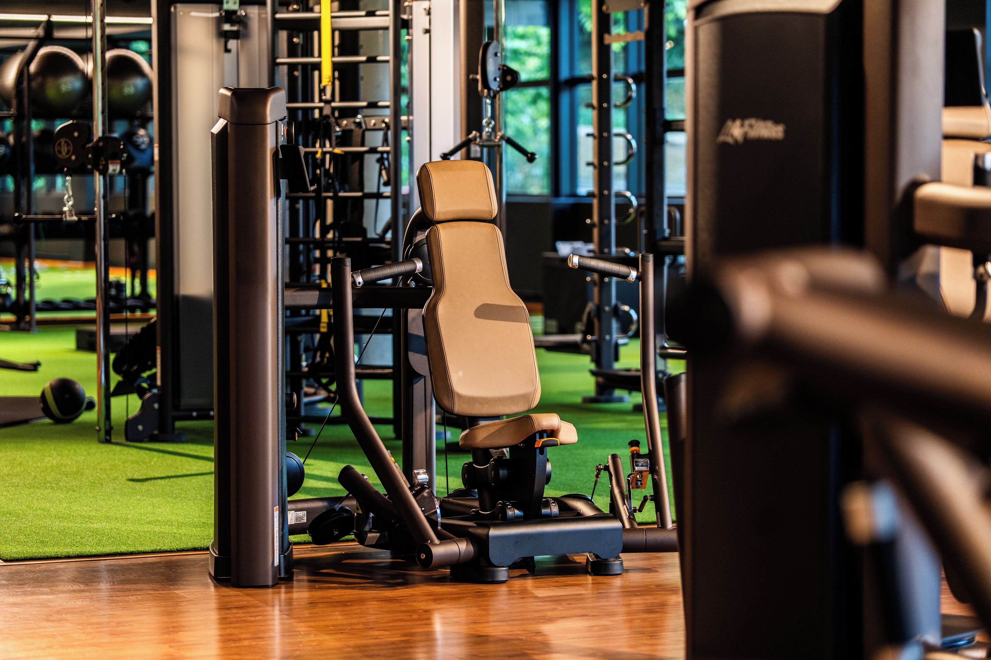 Un gimnasio con equipamiento de ejercicio, suelo de césped artificial verde y un amplio ventanal al fondo.