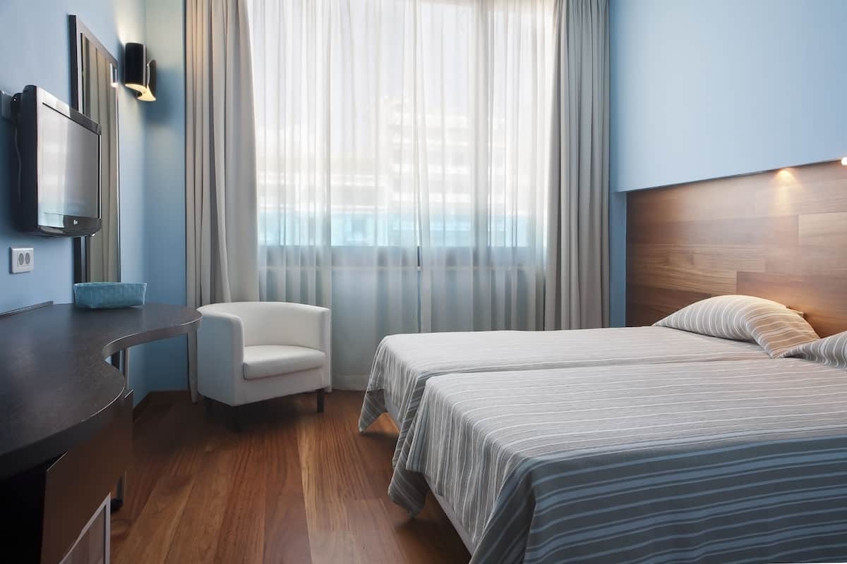 A hotel room with a bed, a desk, a chair, a TV, and a window with curtains.