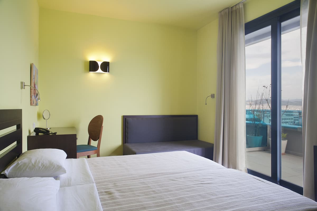 A hotel room with a bed, a desk, a chair, and a view of the outside.