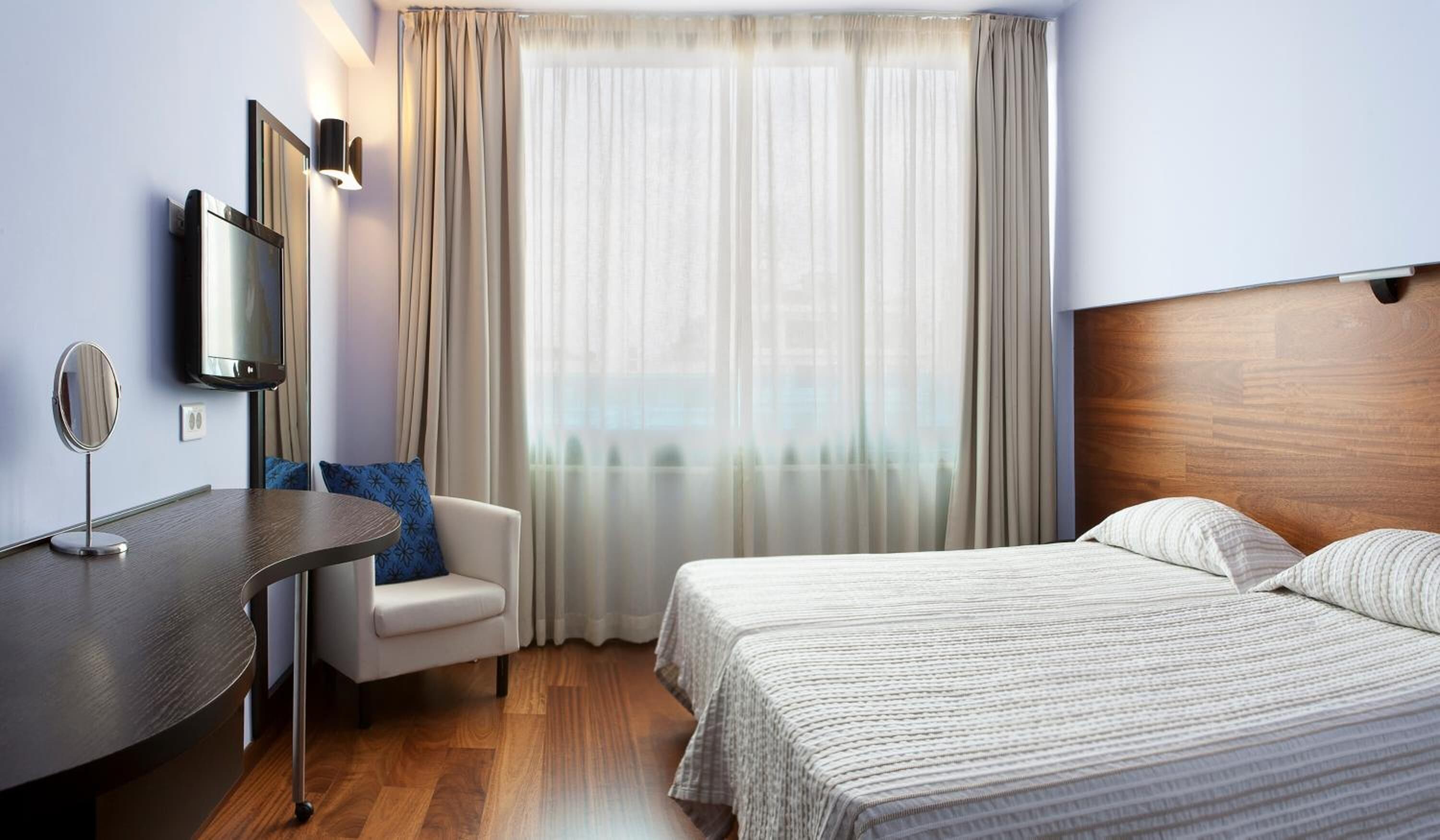 A hotel room with a bed, a desk, a chair, a TV, and a window with curtains.