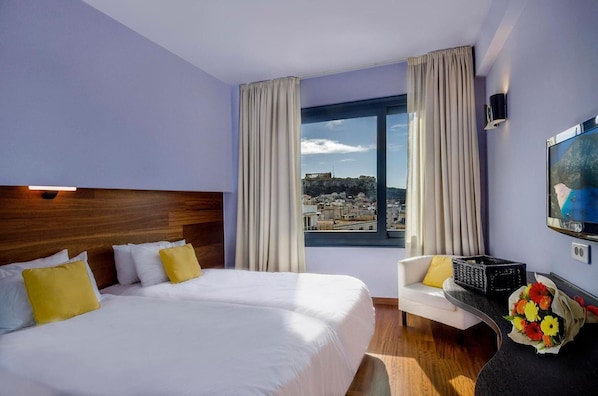 A hotel room with a large bed, a sofa, a TV, and a window with a city view.