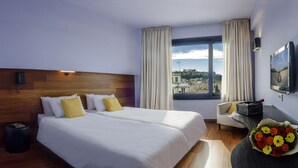 A hotel room with two beds, a view of the city, a desk with a chair, and a vase of flowers. - Athens Center Square Hotel (Athens)