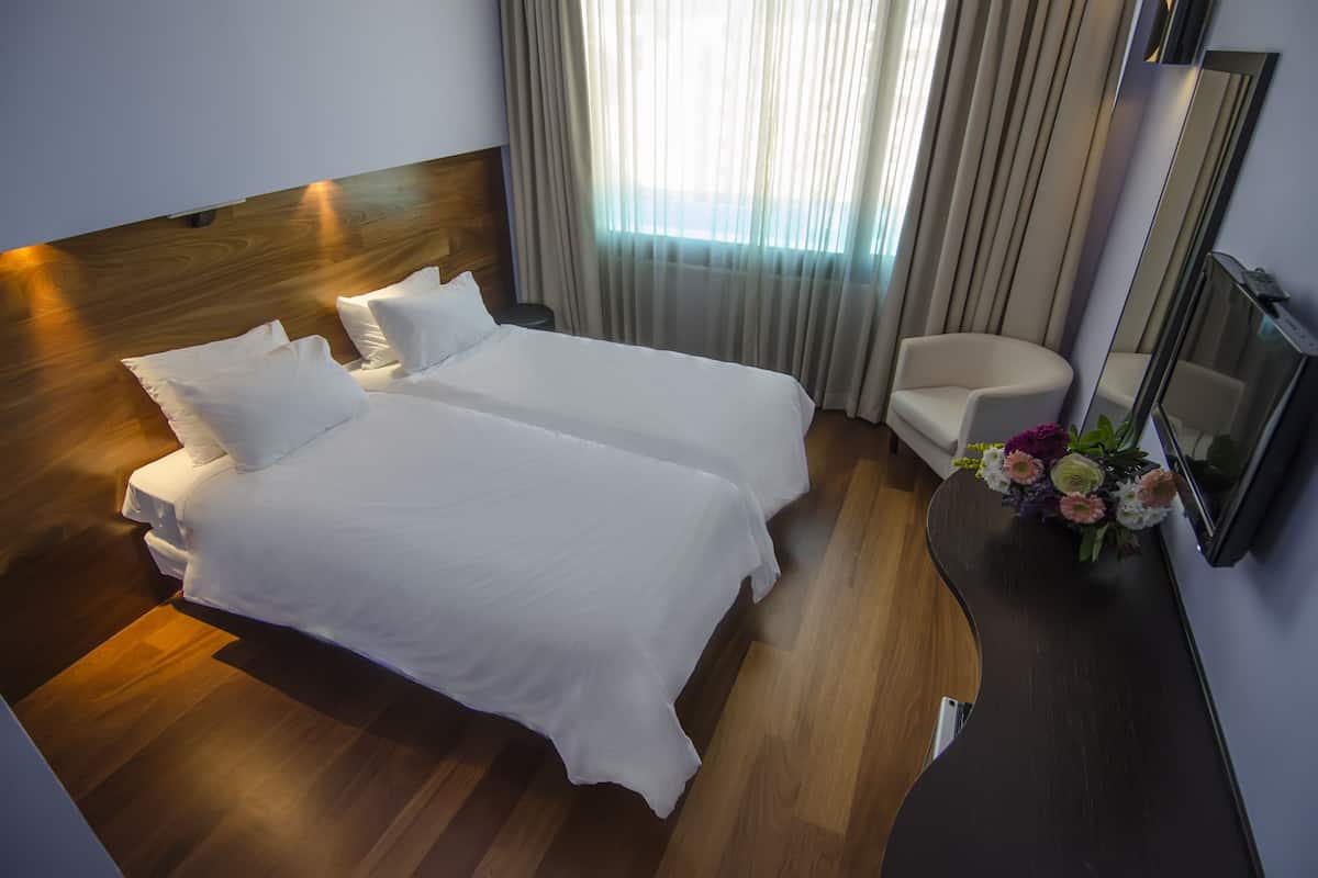 A hotel room with two beds, a wooden headboard, a chair, a mirror, and a vase with flowers.