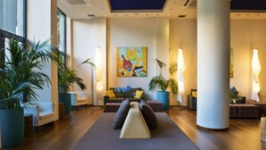 A modern lobby with a sofa, chairs, potted plants, and a colorful abstract painting on the wall. - Athens Center Square Hotel (Athens)
