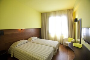 Hotellihuone, jossa on kaksi sänkyä, sohva, pieni pöytä ja peili.