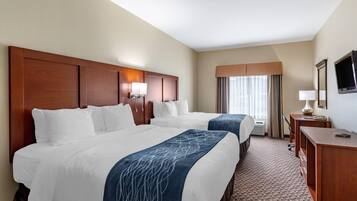 A hotel room with two beds, a desk, a TV, and a window with curtains.