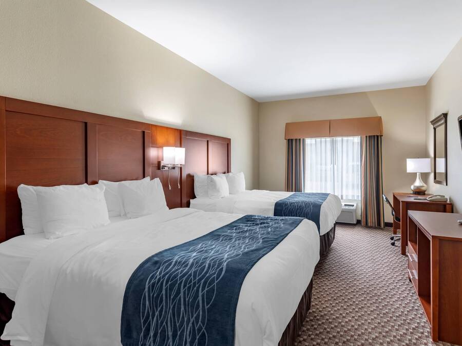 A hotel room with two beds, a desk, a TV, and a window with curtains.
