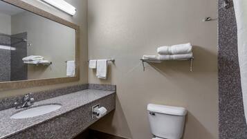 Un baño con lavamanos de encimera de granito, inodoro, toallero y espejo.
