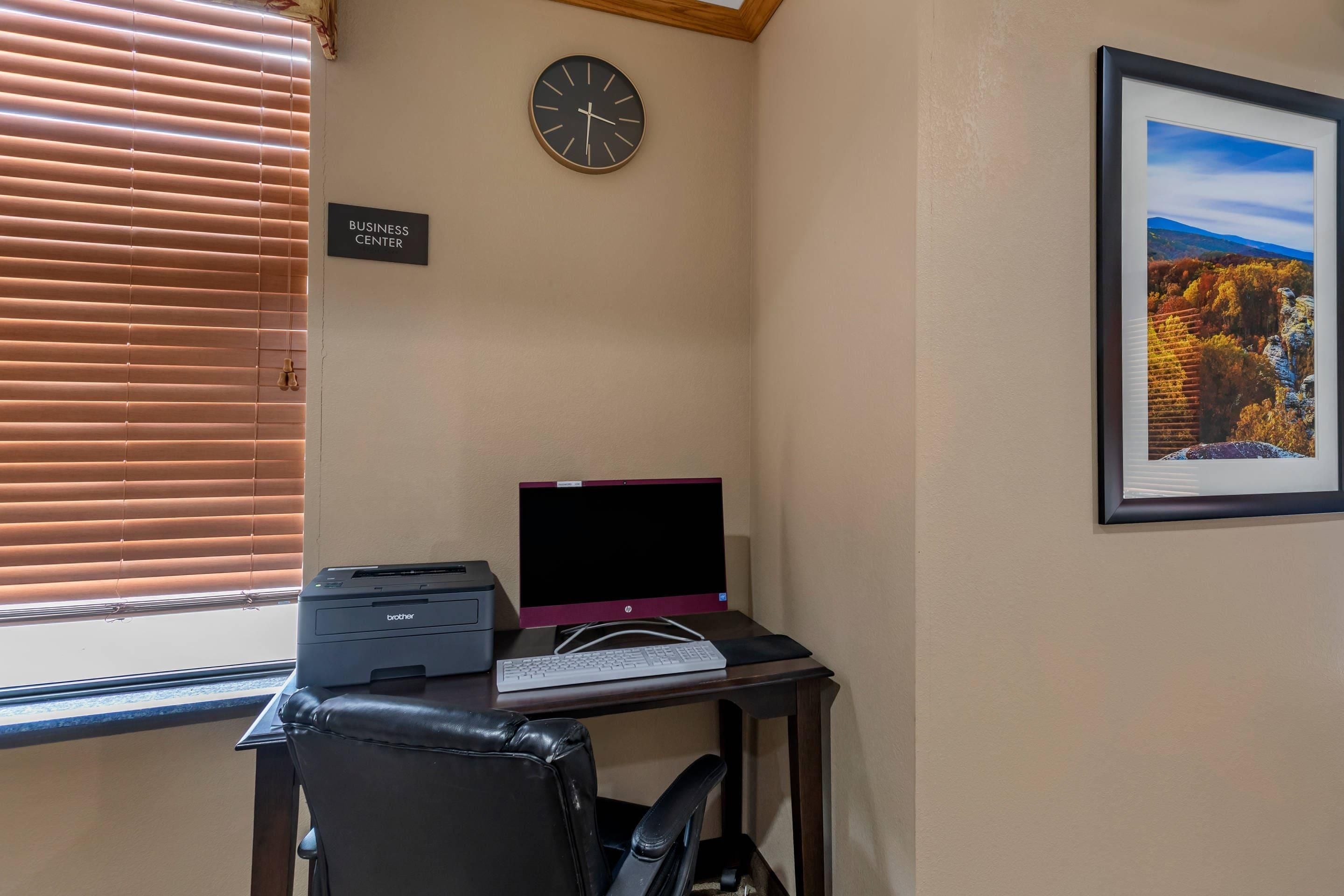 Un espacio de trabajo con un escritorio, una computadora portátil, una impresora, un reloj y un cuadro en la pared.