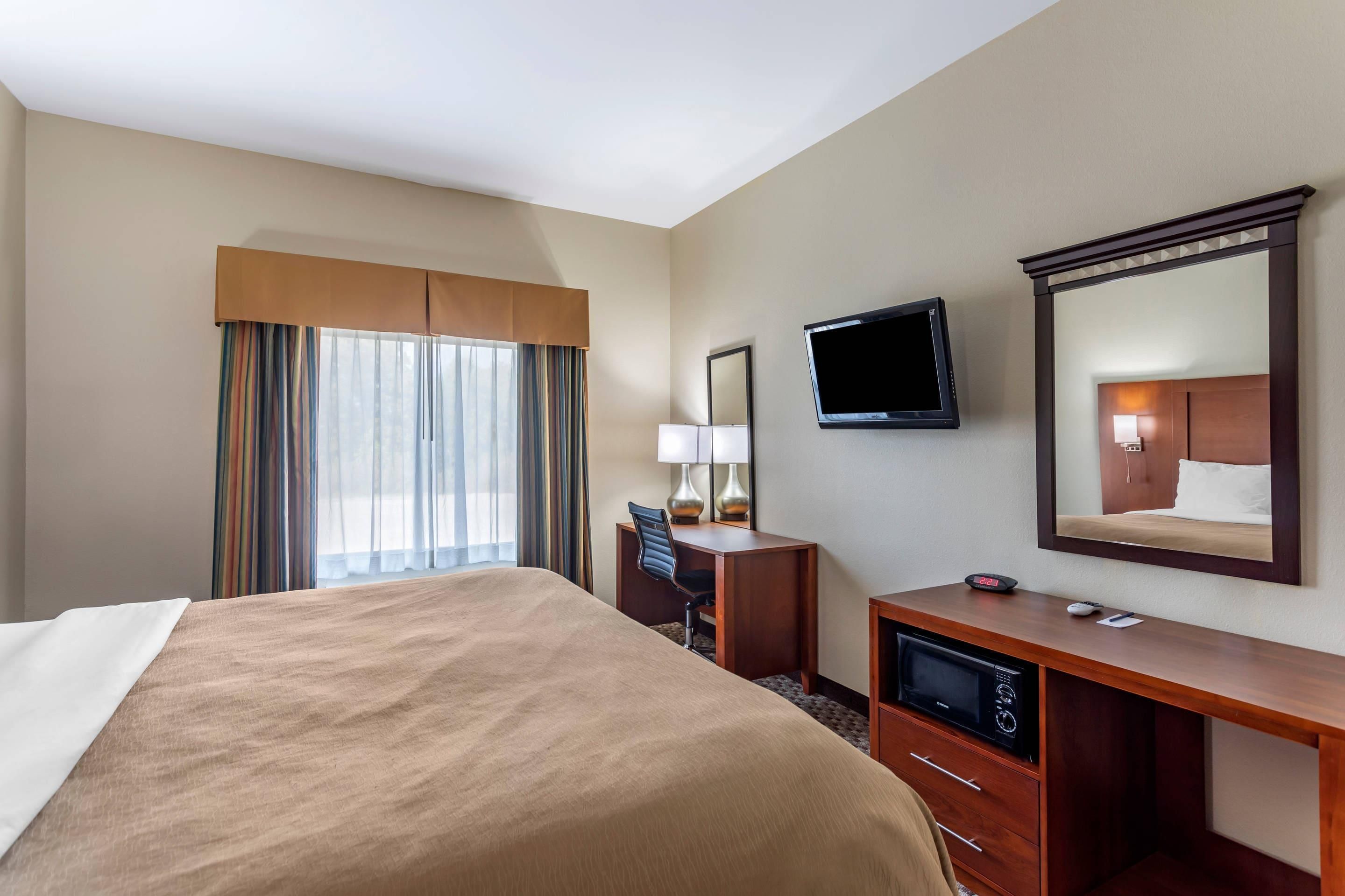 Una habitación de hotel con cama, escritorio, televisión y espejo.