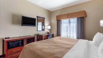 A hotel room with a large bed, a desk with a telephone, a flat-screen TV, a mirror, and a window with curtains.
