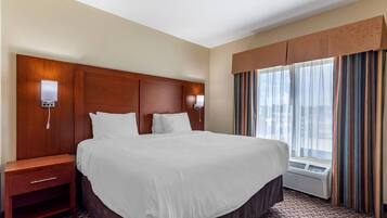 A hotel room with a large bed, bedside tables, a nightstand, a window with curtains, and an air conditioning unit.