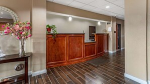 A reception area with a wooden reception desk, a mirror, and a vase with flowers. - Comfort Inn & Suites Carbondale University Area (Carbondale)
