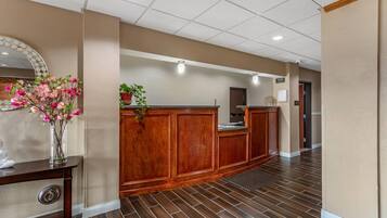 A reception area with a wooden reception desk, a potted plant, and a vase with flowers.
