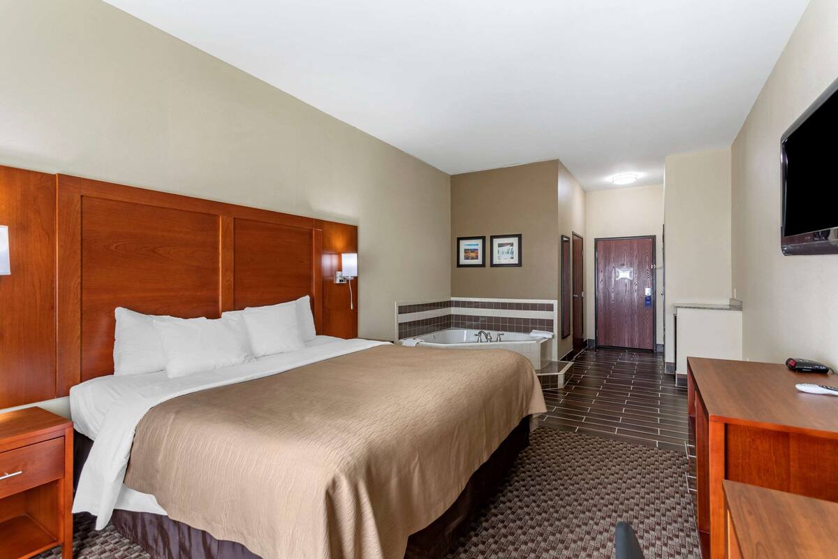 A hotel room with a large bed, a separate bathroom with a bathtub, a desk, and a television.