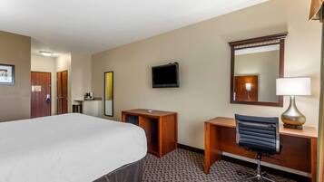 A hotel room with a bed, a desk, a chair, a television, a mirror, and a lamp.