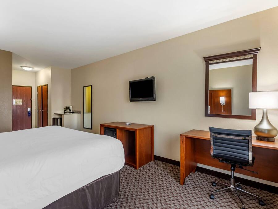 A hotel room with a bed, a desk, a chair, a television, a mirror, and a lamp.