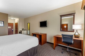 Habitación de hotel con cama, escritorio, silla, televisor, espejo y lámpara.