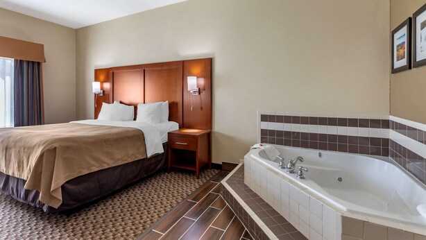 A hotel room with a large bed, a wooden headboard, two bedside lamps, a nightstand, and a separate bathroom with a bathtub. - Comfort Inn & Suites Carbondale University Area (Carbondale)