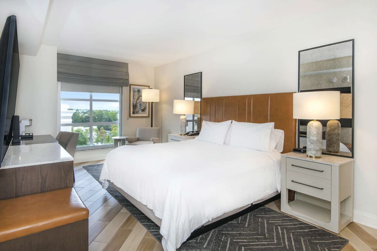 Habitación de hotel con una cama grande, mesitas de noche con lámparas, un escritorio y vistas al exterior.