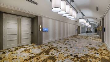 A hotel corridor with a patterned carpet, white doors, and modern lighting fixtures.