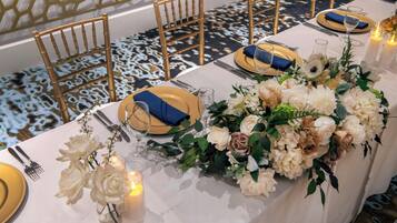 Ein Bankettisch mit gold- und blauem Geschirr, einer weißen Tischdecke und floralen Mittelpunkten.