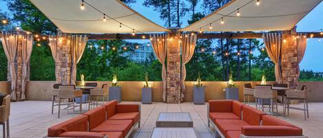 An outdoor patio area with wicker furniture, stone pillars, and string lights.