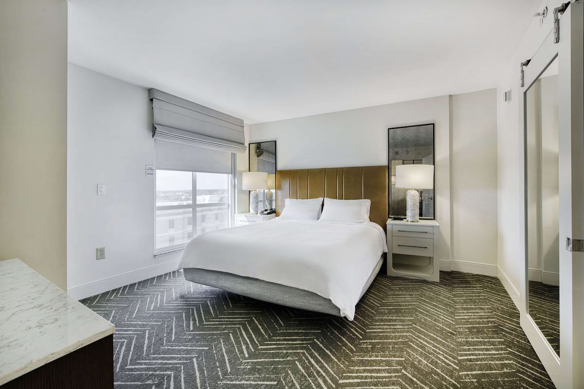 Habitación de hotel con una cama grande, lámparas de noche, un escritorio y vistas a la ciudad.