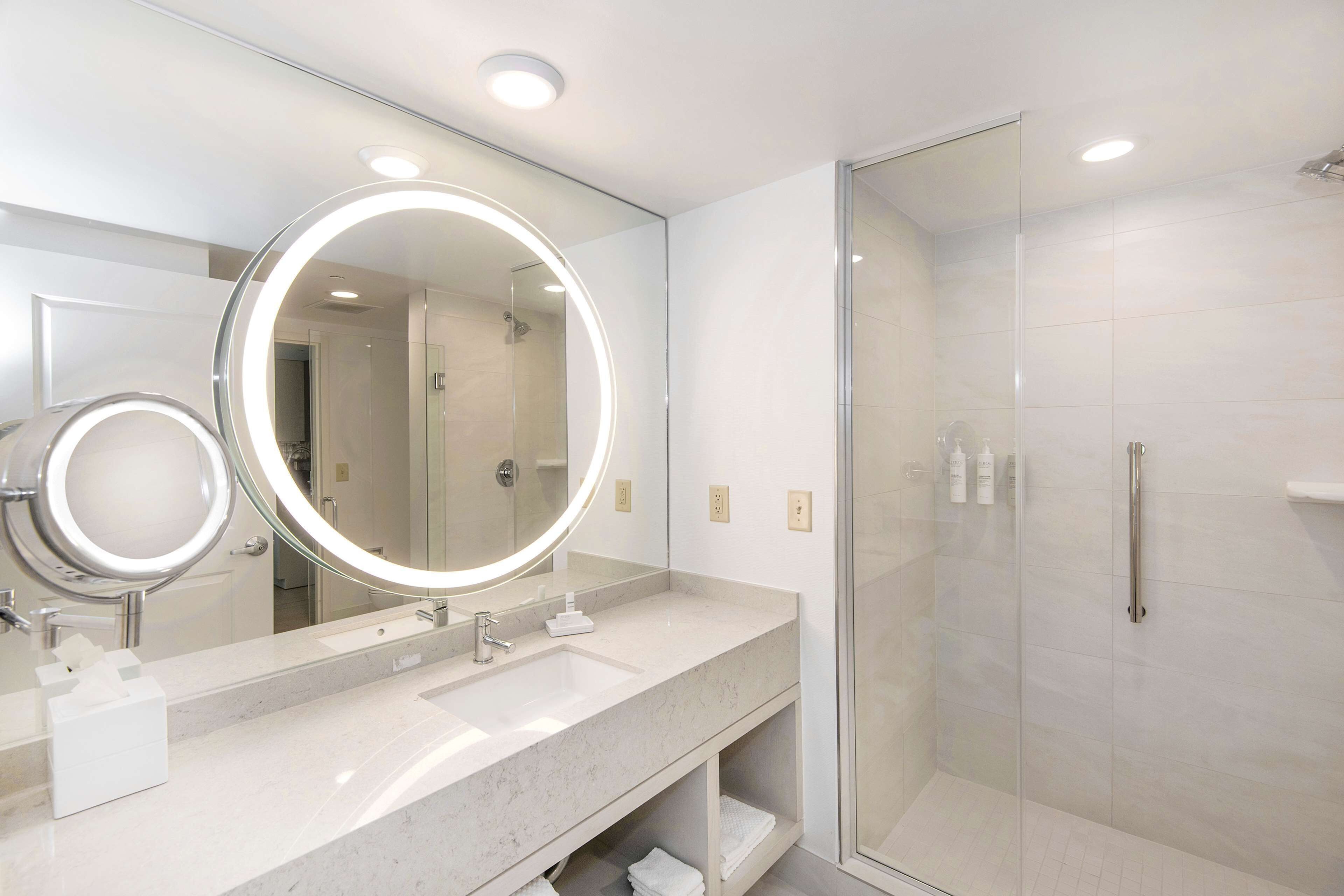 A modern bathroom with a large mirror, a glass-enclosed shower, and a marble countertop.