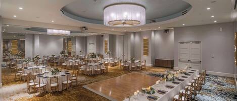 Ein großer Festsaal mit runden Tischen und einem langen Tisch, alle mit weißen Tischdecken und floralen Mittelstücken gedeckt.