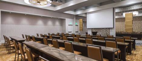 A conference room with long tables and chairs, a projector screen, and a decorative wall.