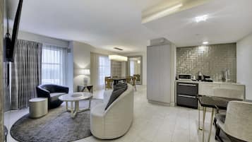 A modern living room with a sofa, armchair, and coffee table, a dining area with chairs, and a kitchen with appliances.