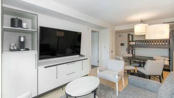 A modern living room with a flat-screen TV, a dining area with a table and chairs, and a sofa.