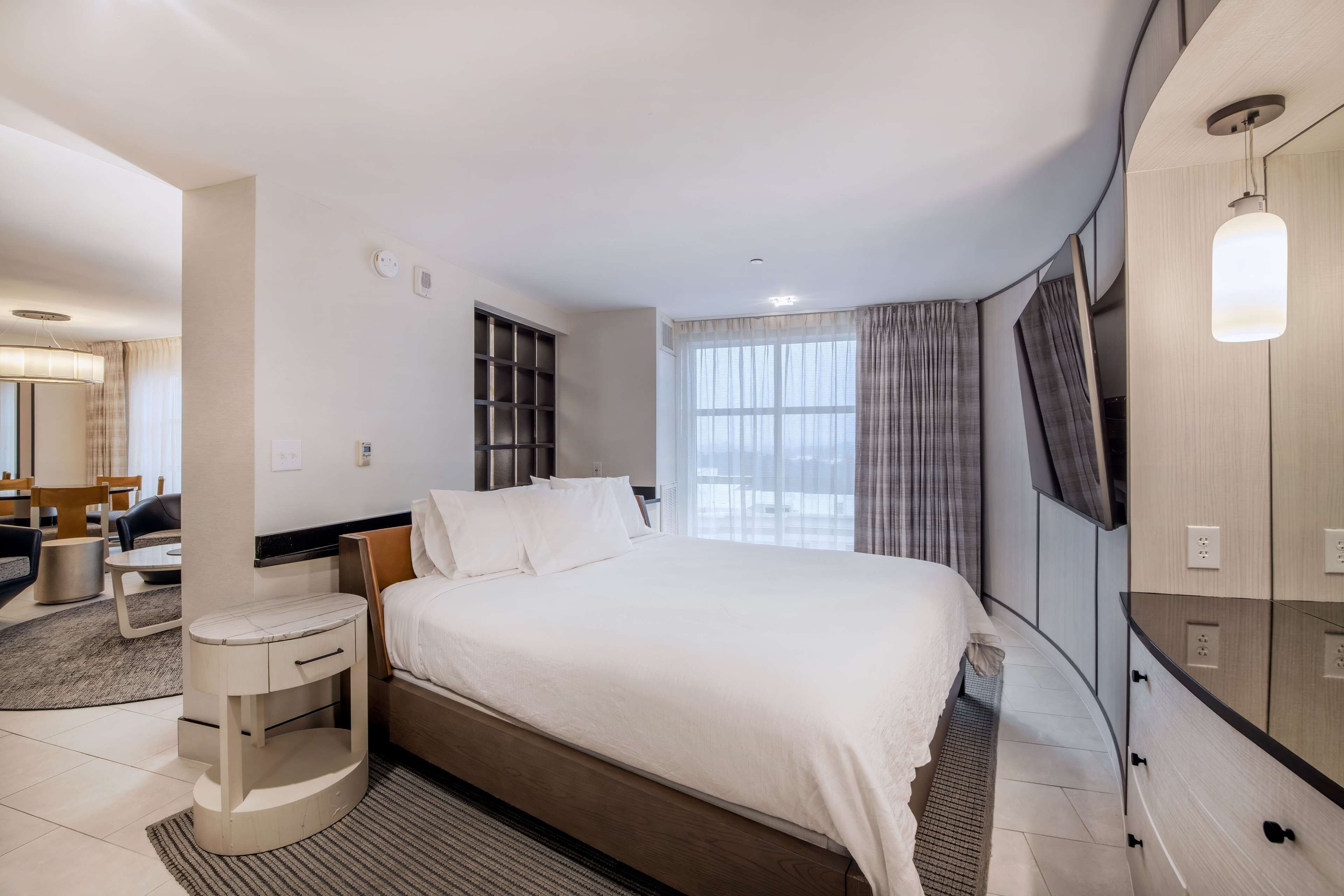 A modern hotel room with a large bed, a bedside table, a TV, and a wardrobe.