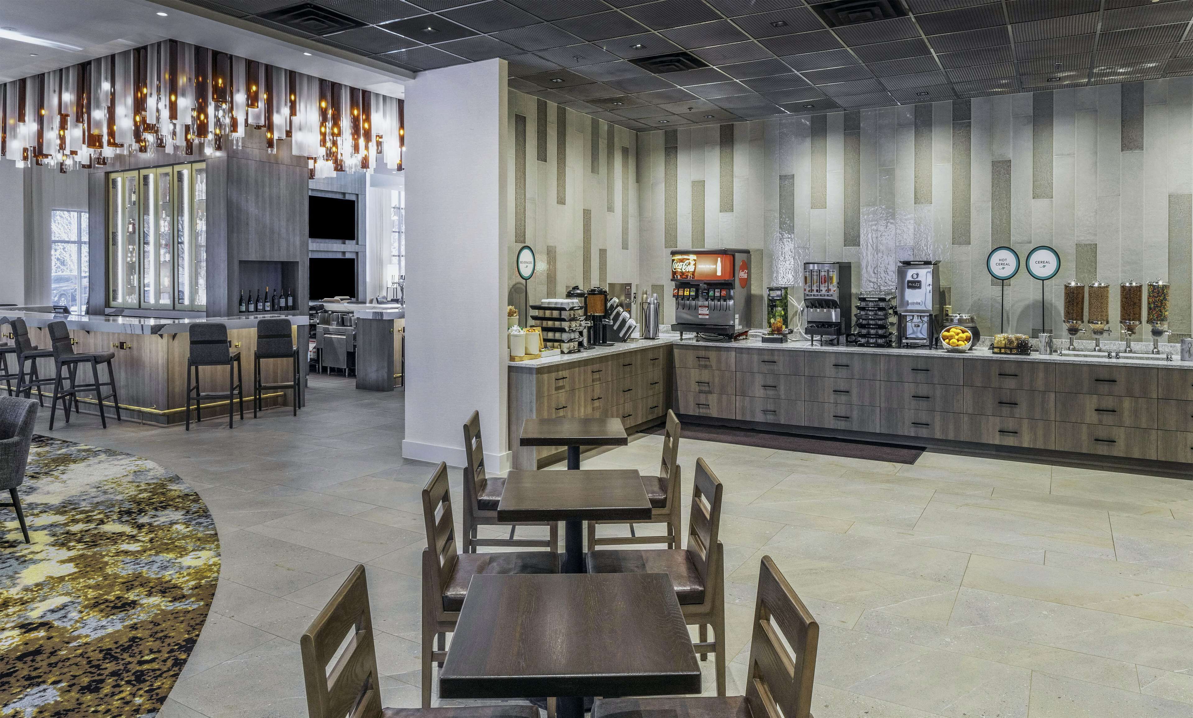 A modern restaurant with a bar area, seating, and a kitchen in the background.