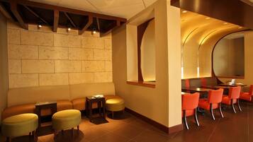 A hotel lobby with a seating area, a reception desk, and a conference room with orange chairs.