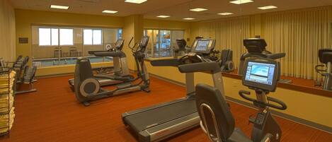 Un gimnasio con cintas de correr, elípticas y un espejo grande.