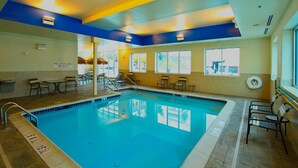 An indoor swimming pool with clear water, surrounded by lounge chairs and tables.