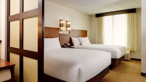 A hotel room with two beds, a wooden headboard, a bedside table, and a lamp.