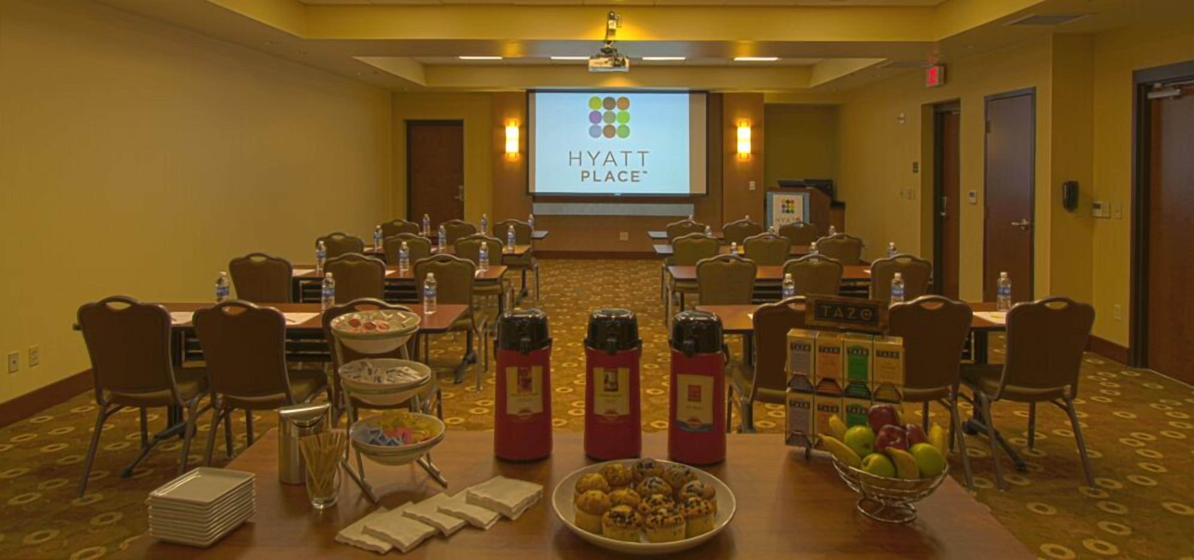A conference room with multiple tables, chairs, and a projector screen displaying the Hyatt Place logo.