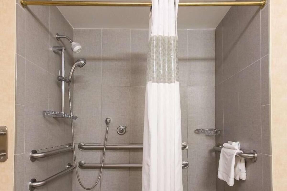A shower area with a white curtain, grab bars, and a towel rack.