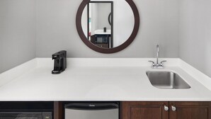 A modern kitchen with a white countertop, a built-in dishwasher, a coffee maker, a sink, and a mirror with a dark frame. - Hampton Inn & Suites Parsippany/North (Parsippany)
