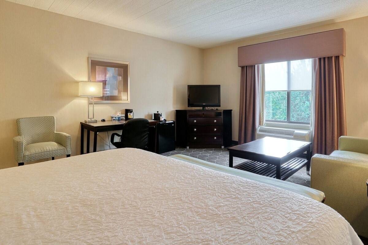 A hotel room with a large bed, a desk with a chair, a television, and a window with curtains.