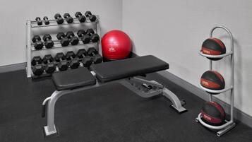 A gym with a bench, dumbbells, a red medicine ball, and a wall-mounted medicine ball rack.