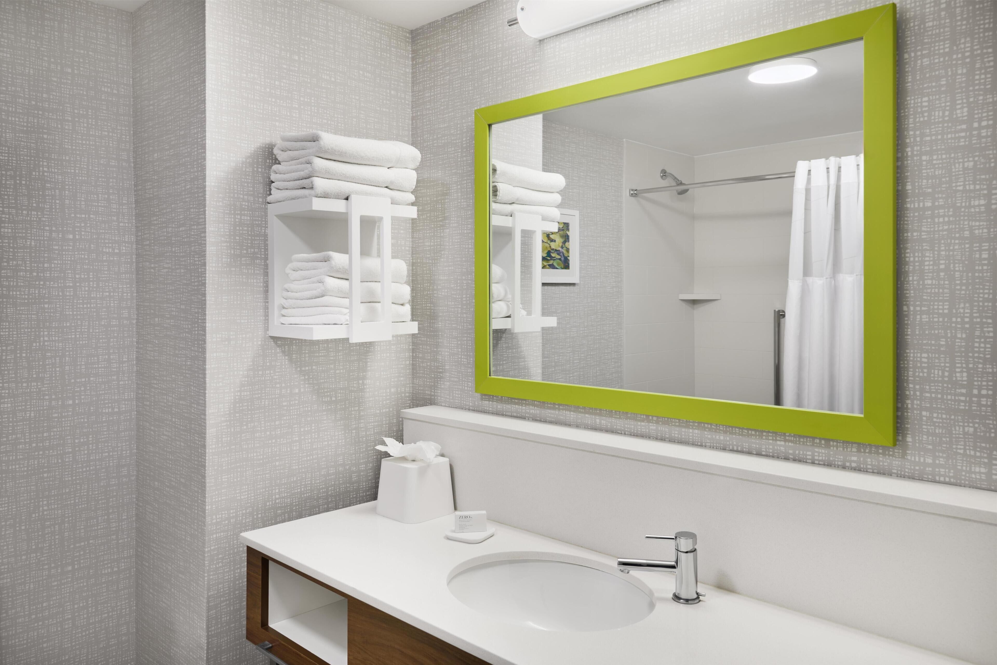 Un baño con un lavabo blanco, un espejo con marco verde y toallas ordenadas.