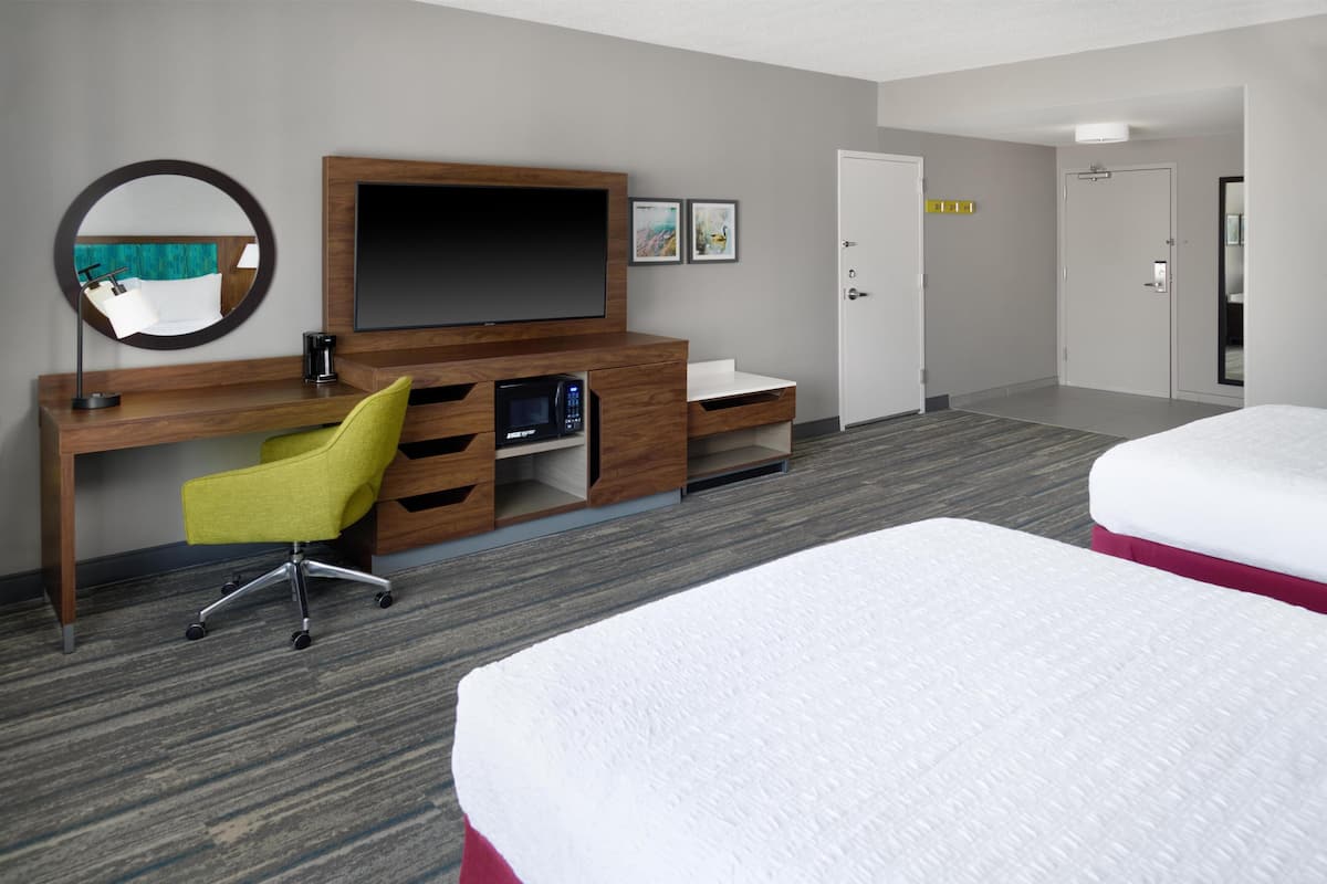 A hotel room with a wooden desk, a flat-screen TV, a yellow chair, a bed, and a door.