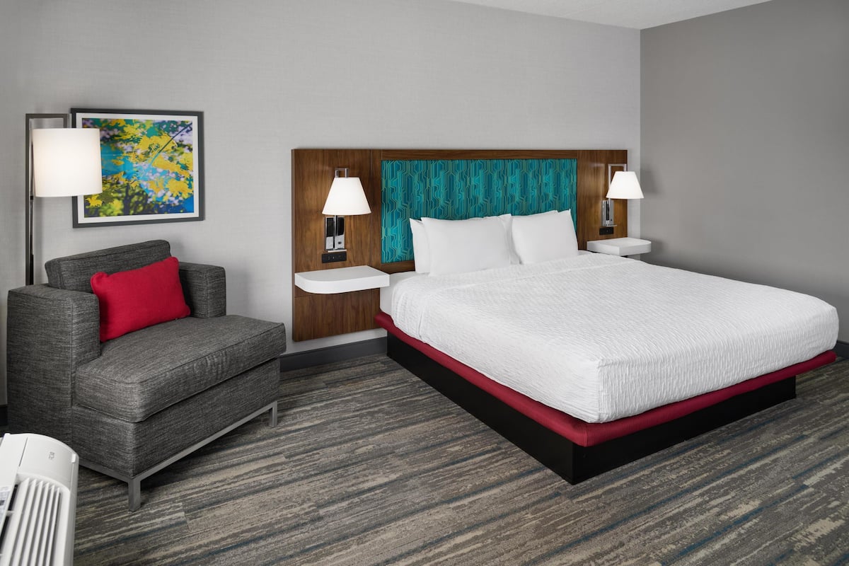 A hotel room with a bed, a chair, two bedside tables, a lamp, and a framed picture on the wall.